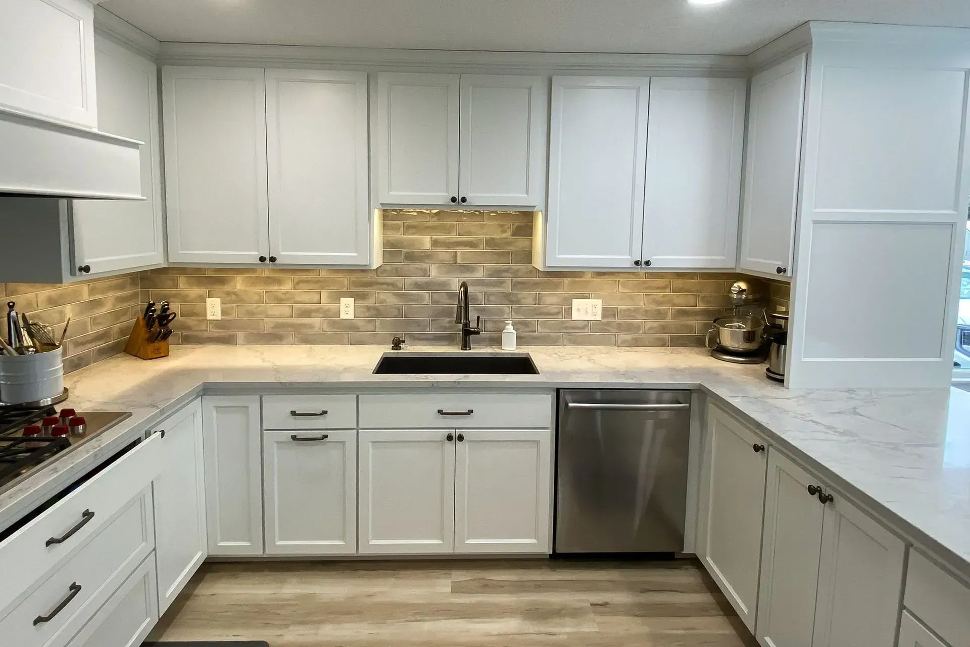 White kitchen with stone backsplash, stainless steel appliances, and dark fixtures.