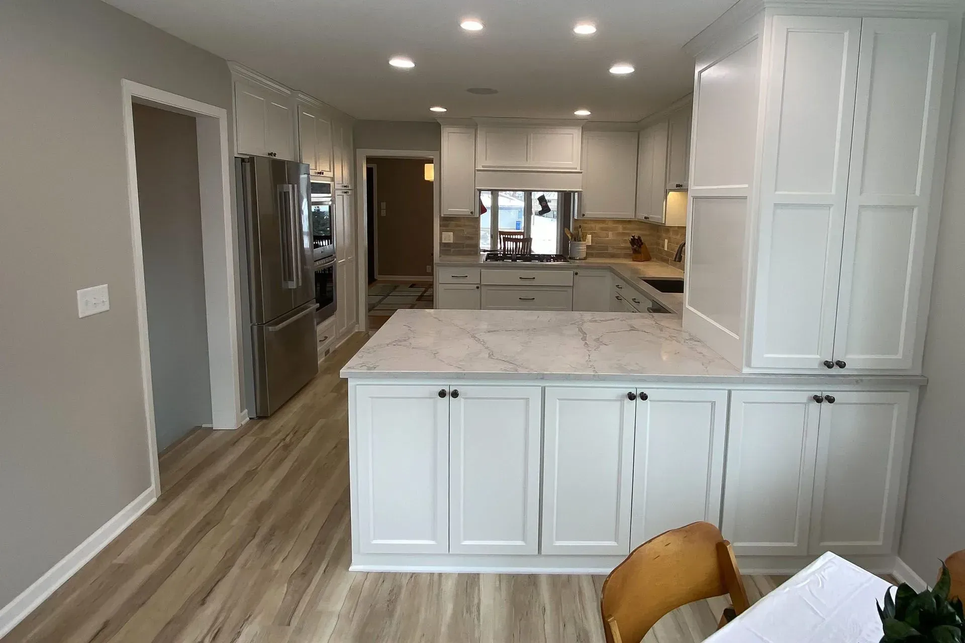 Modern kitchen with white cabinets, light wood floor, and a marble countertop island.