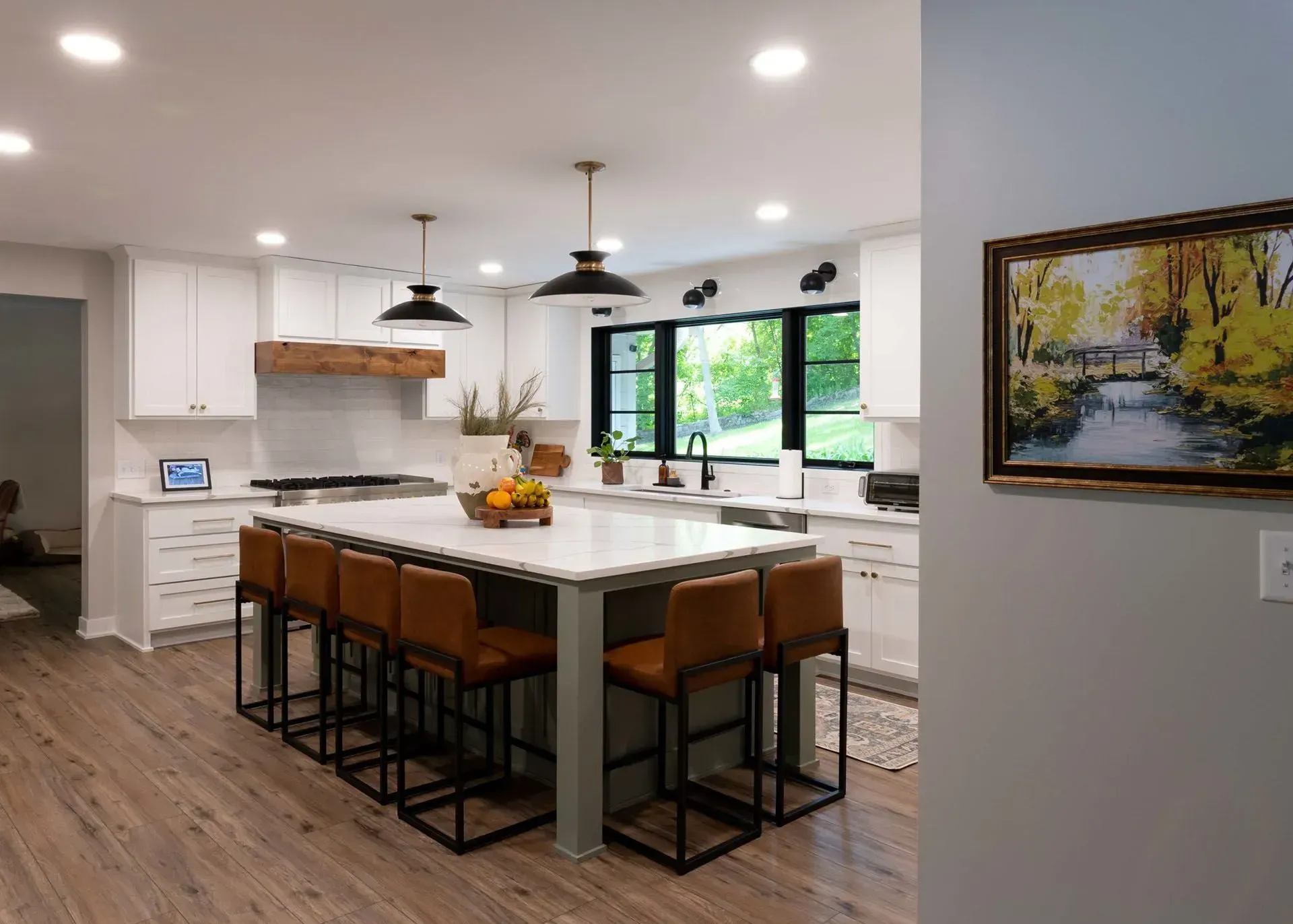 Modern kitchen with white cabinets, large island with brown bar stools, and artwork on the wall.