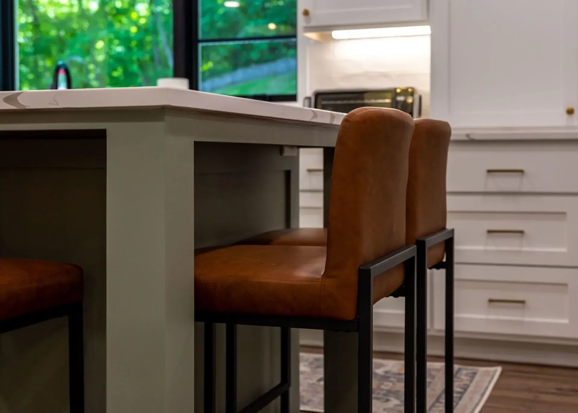 Two brown leather bar stools at a kitchen island, white cabinets in the background.