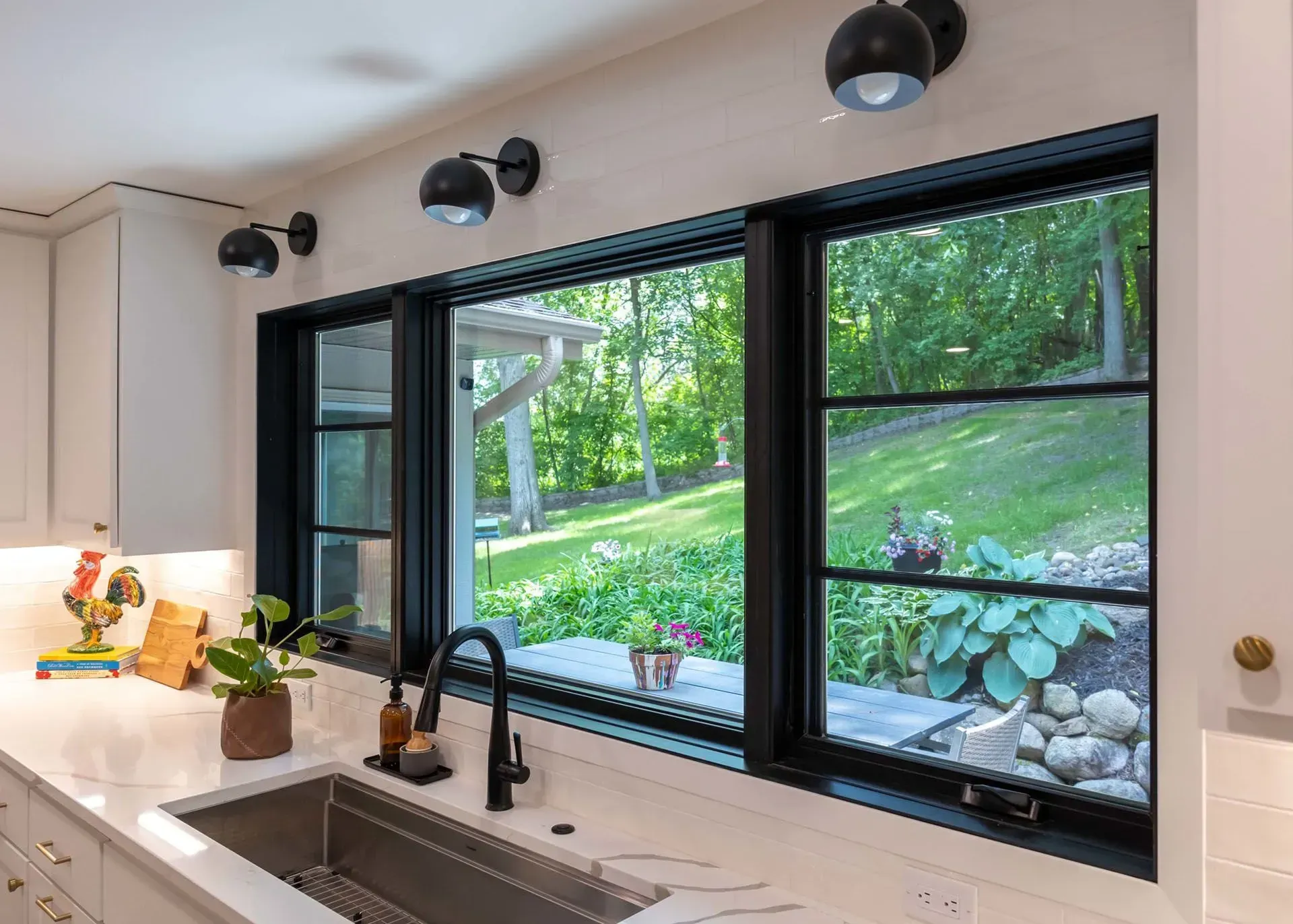 Kitchen with black-framed windows overlooking a green yard, white countertops, and black fixtures.