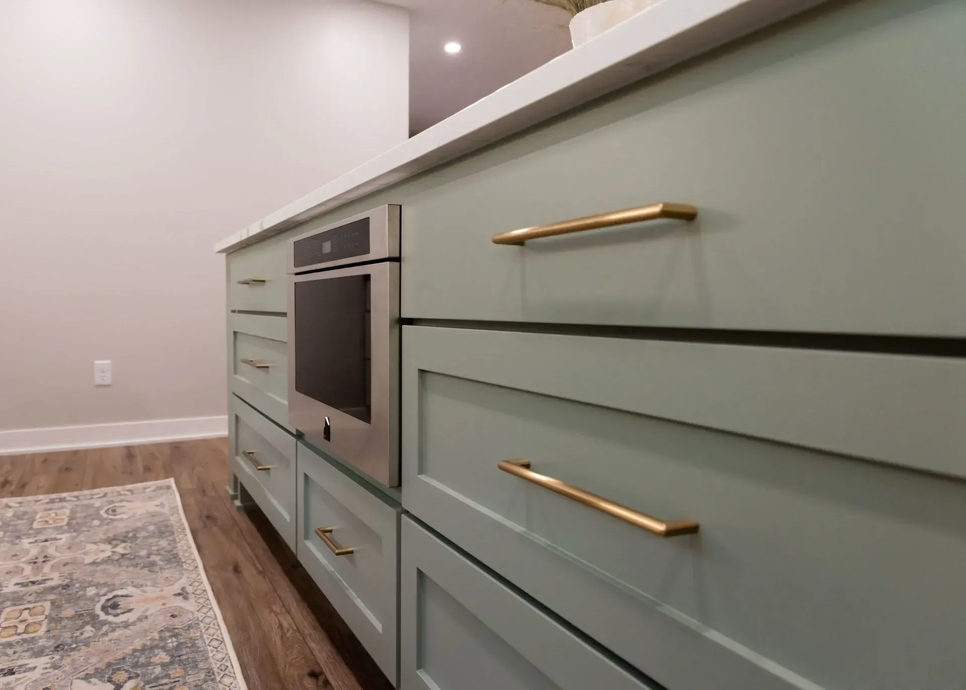 Close-up of a kitchen island with mint-green cabinets, gold hardware, and a built-in oven.