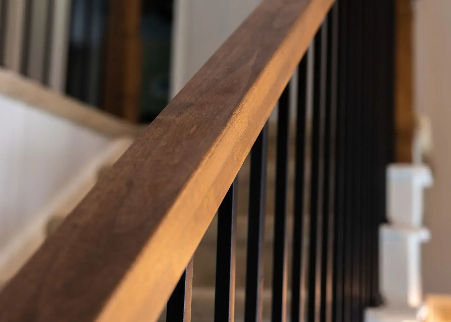 Close-up of a wooden handrail with black metal spindles and white stair trim.