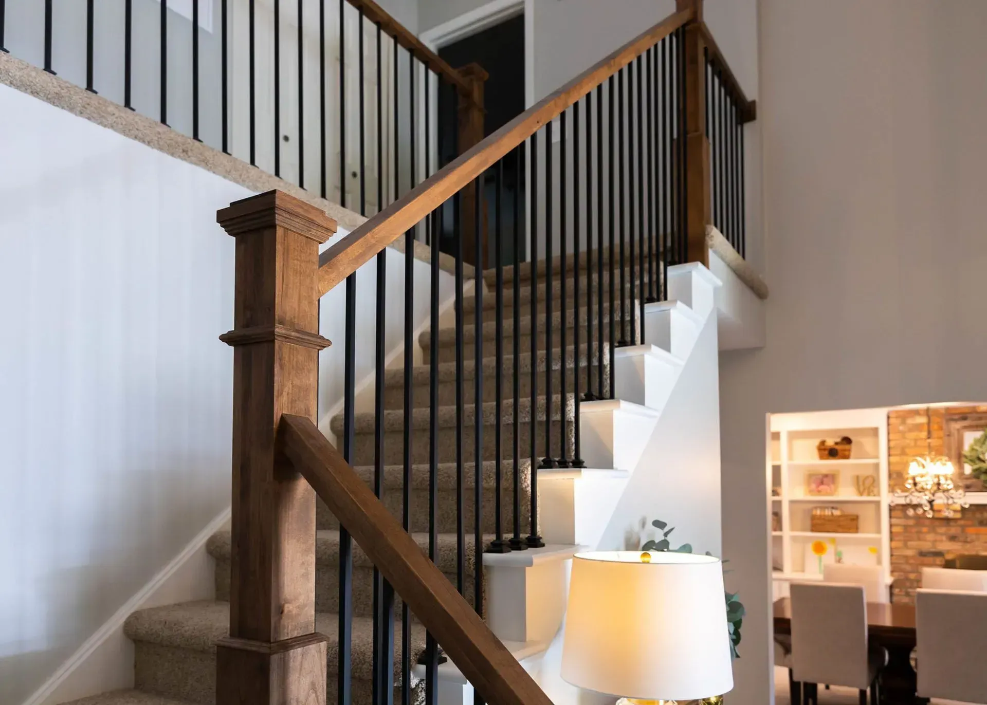 Staircase with wooden handrails, black spindles, and carpeted steps, against a white wall.