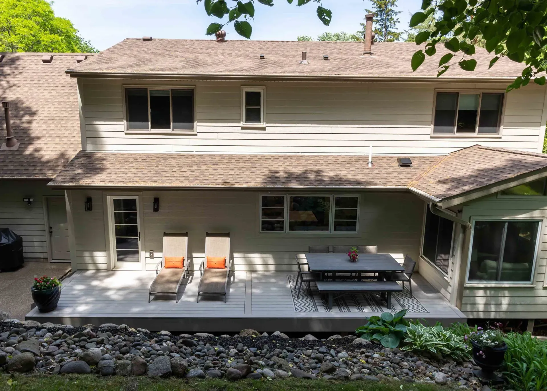 Backyard with a light gray deck, patio furniture, and a house with a brown roof and light green siding.