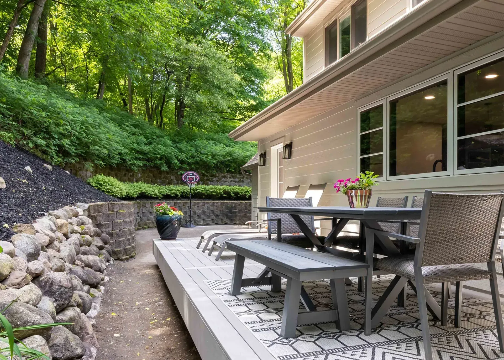 Backyard patio with a table and chairs, adjacent to a sloped hill with lush greenery.