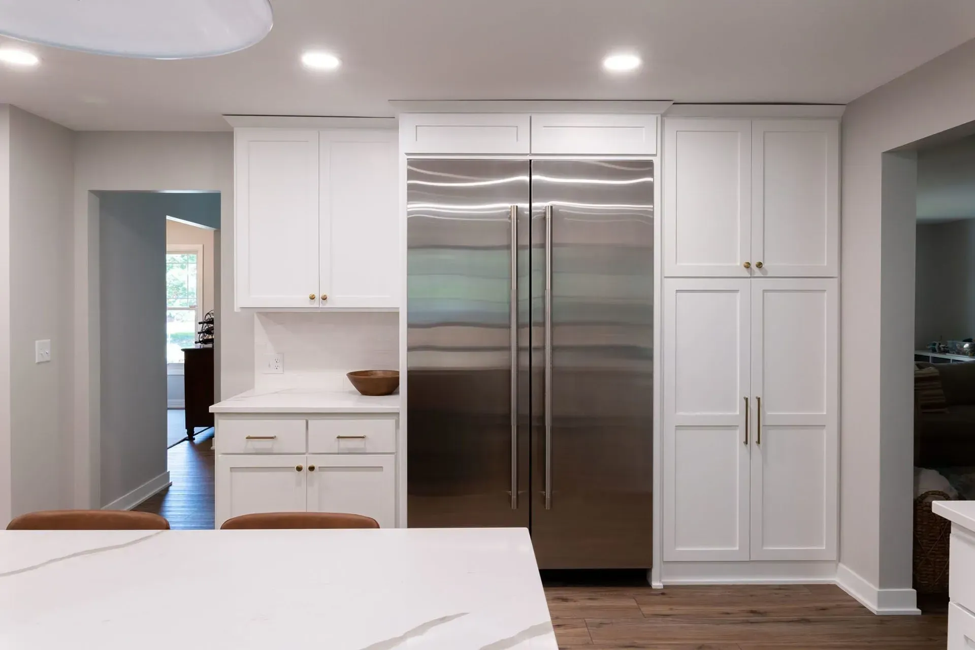 White kitchen with stainless steel refrigerator, cabinets, and a white countertop island.