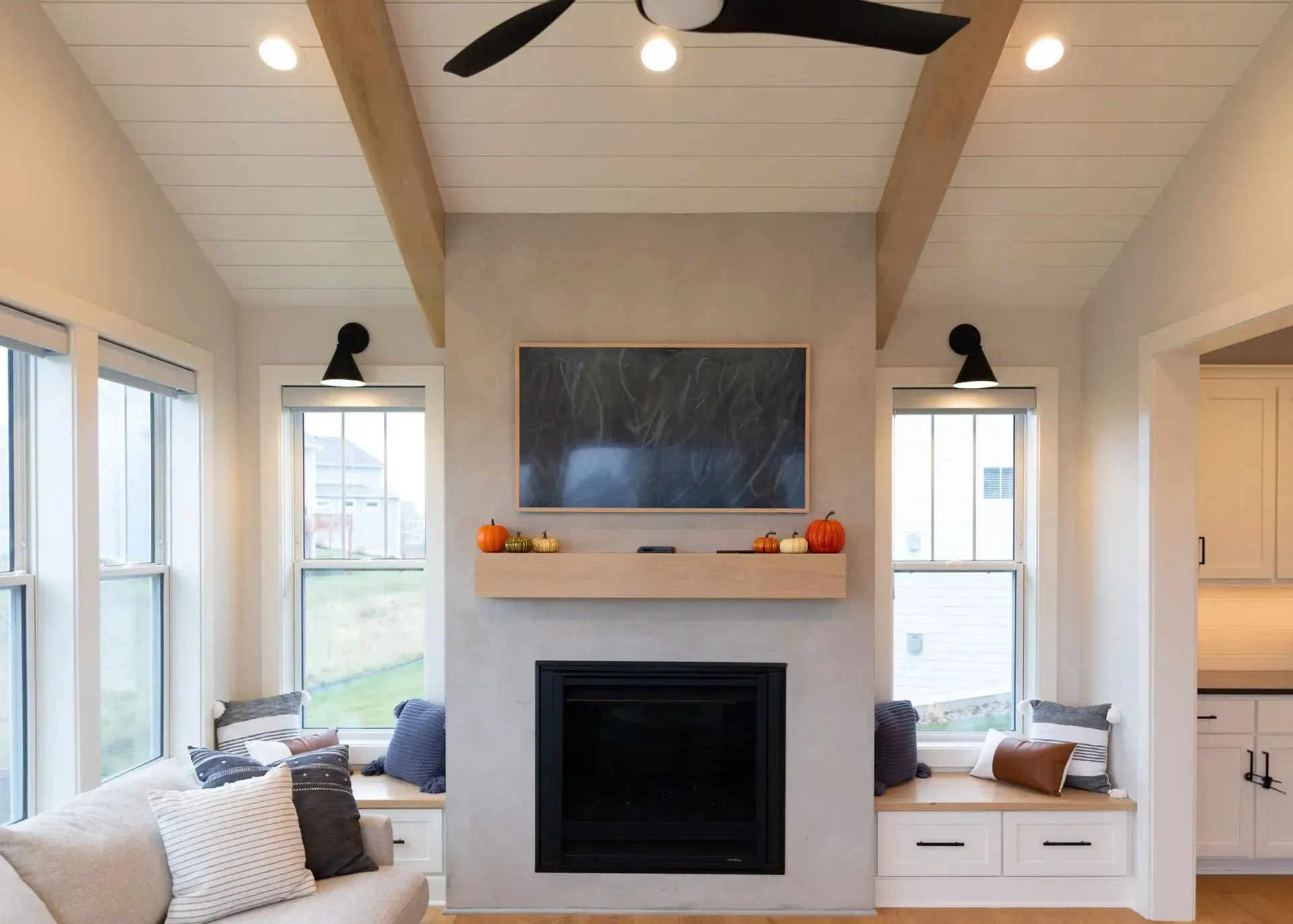 Living room with fireplace, TV, windows, and decorative fall gourds.
