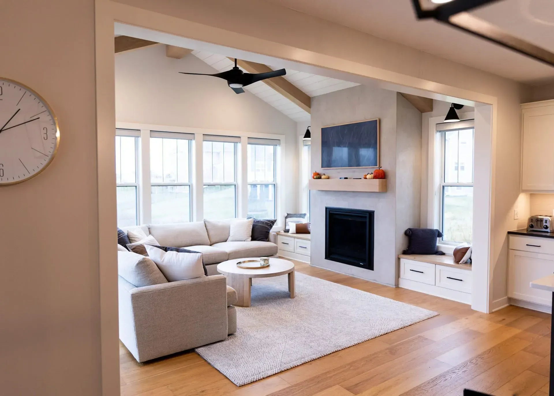 Cozy living room with fireplace, sectional sofa, and large windows.  Neutral tones, light wood floors, and ceiling fan.