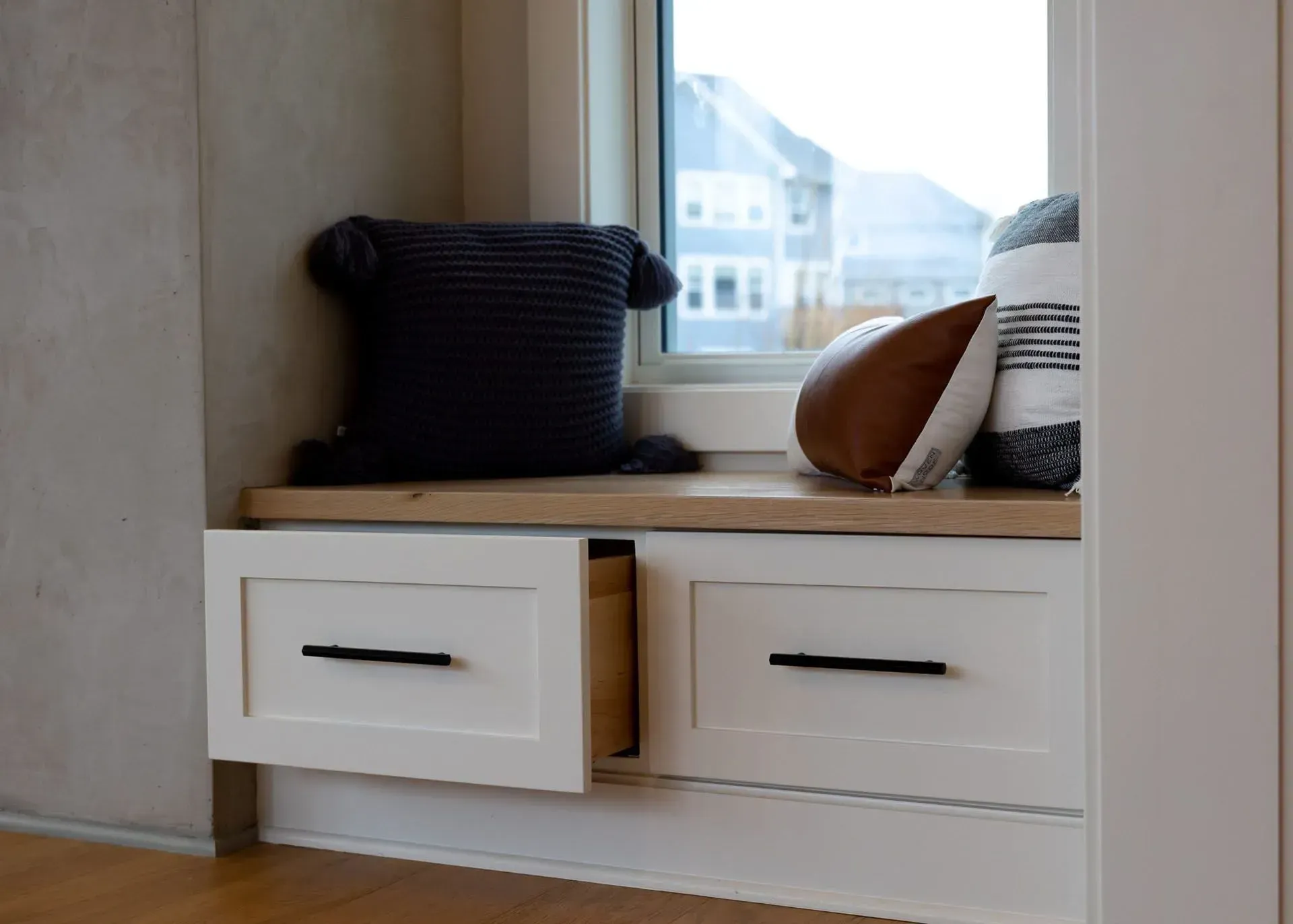 Window seat with two white drawers, a pillow, and a folded blanket.