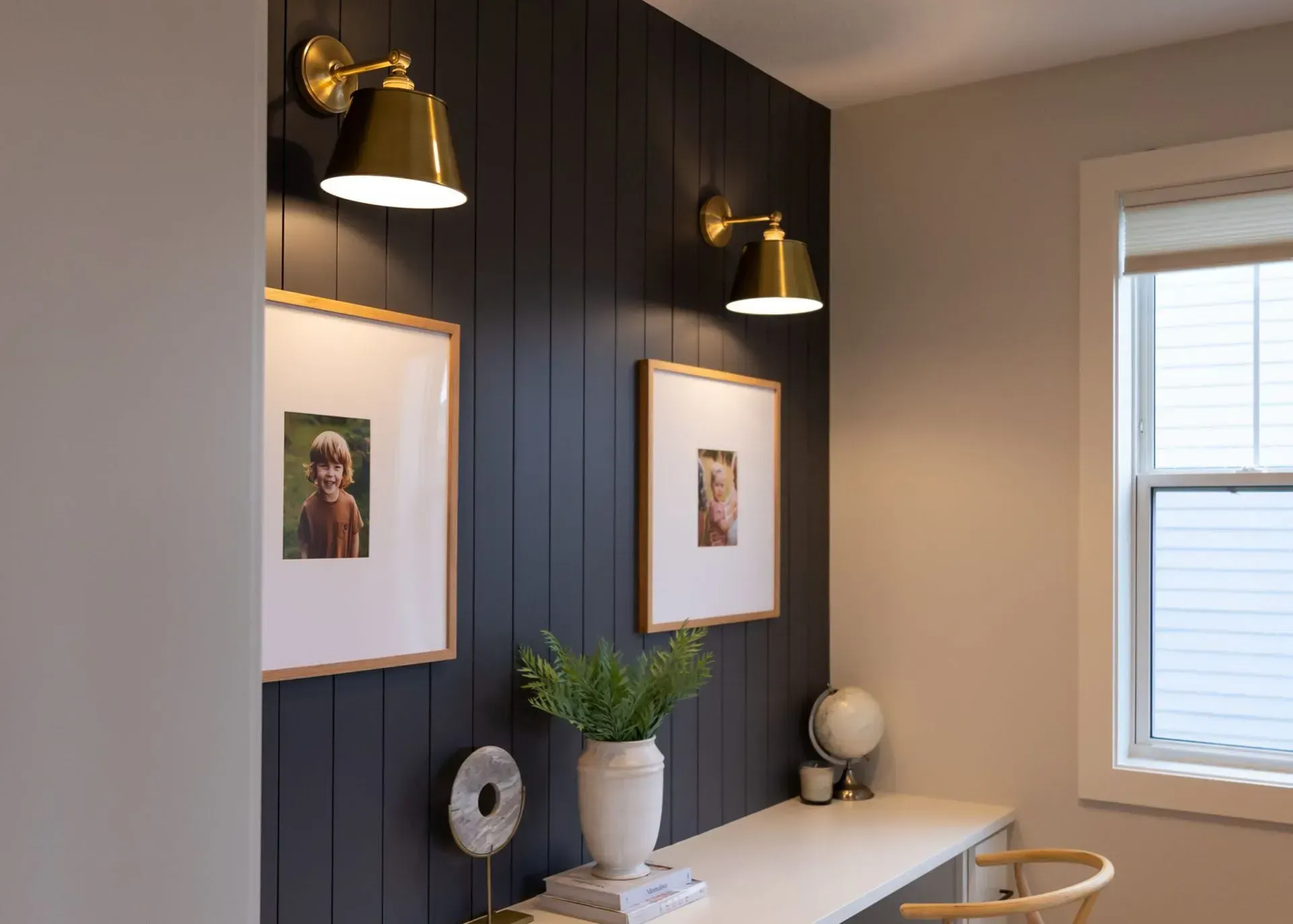 Desk with dark accent wall, two sconce lights, two framed photos, and a white vase.