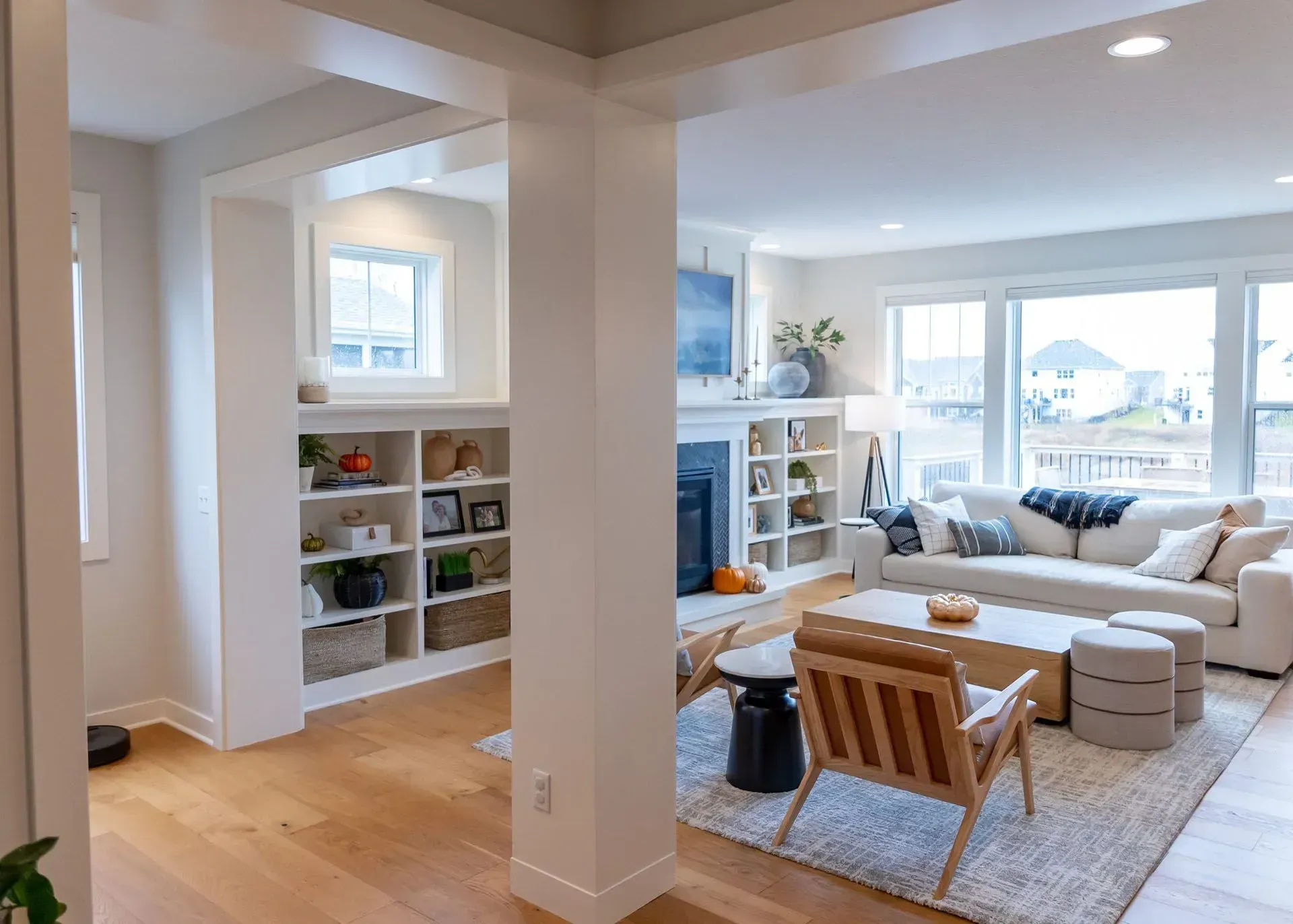 Bright living room with white built-ins, wooden floors, and a couch by a window overlooking a yard.