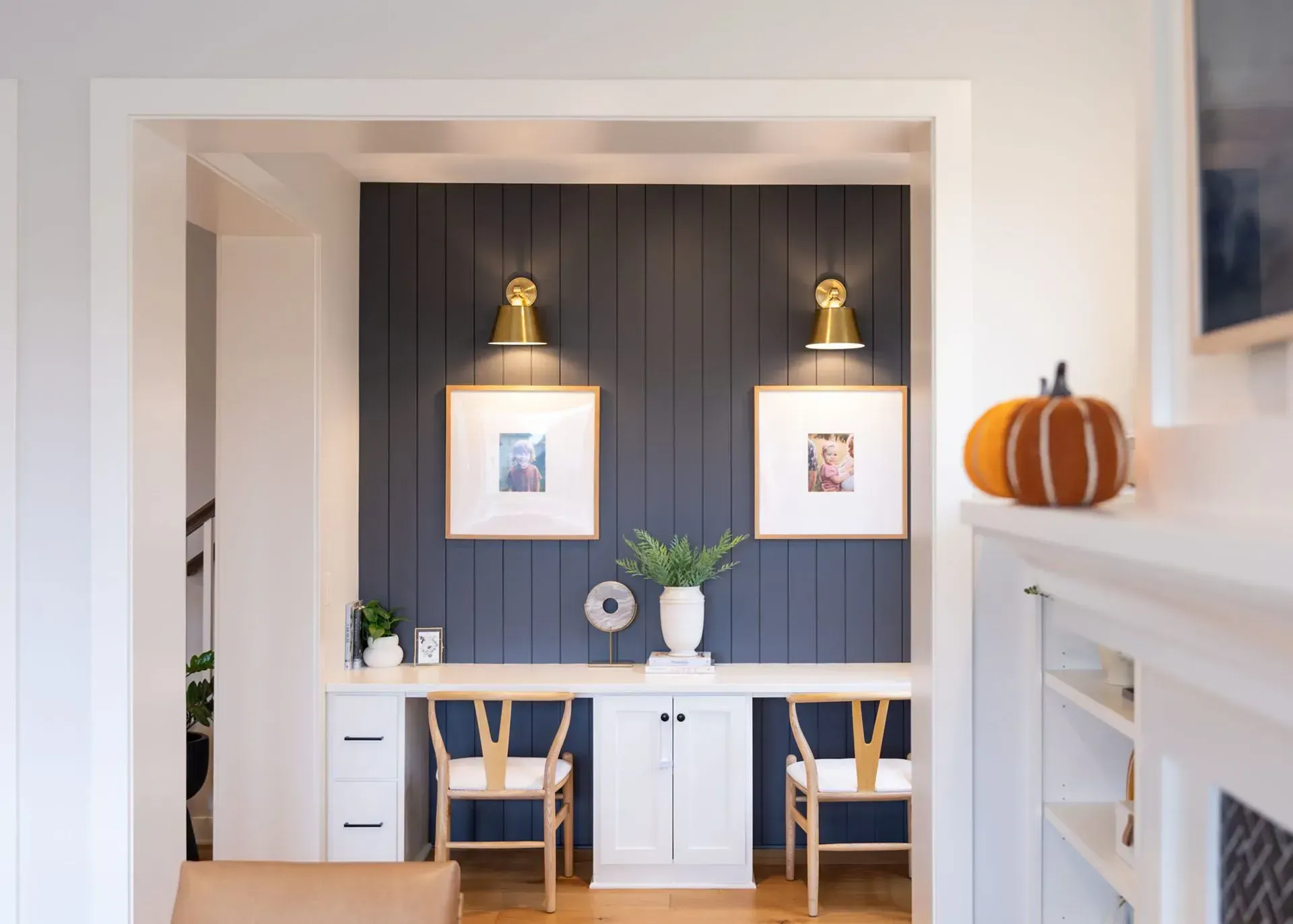 Built-in desk nook with navy shiplap wall, brass sconces, framed photos, and two chairs.