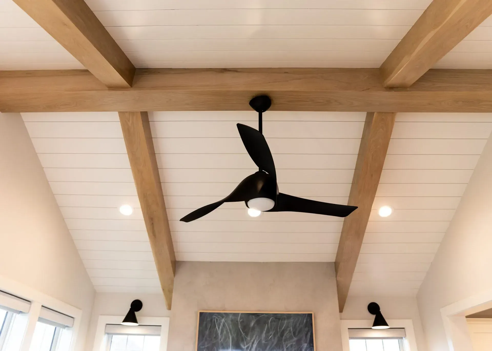 Beamed ceiling with black ceiling fan and white paneled boards.