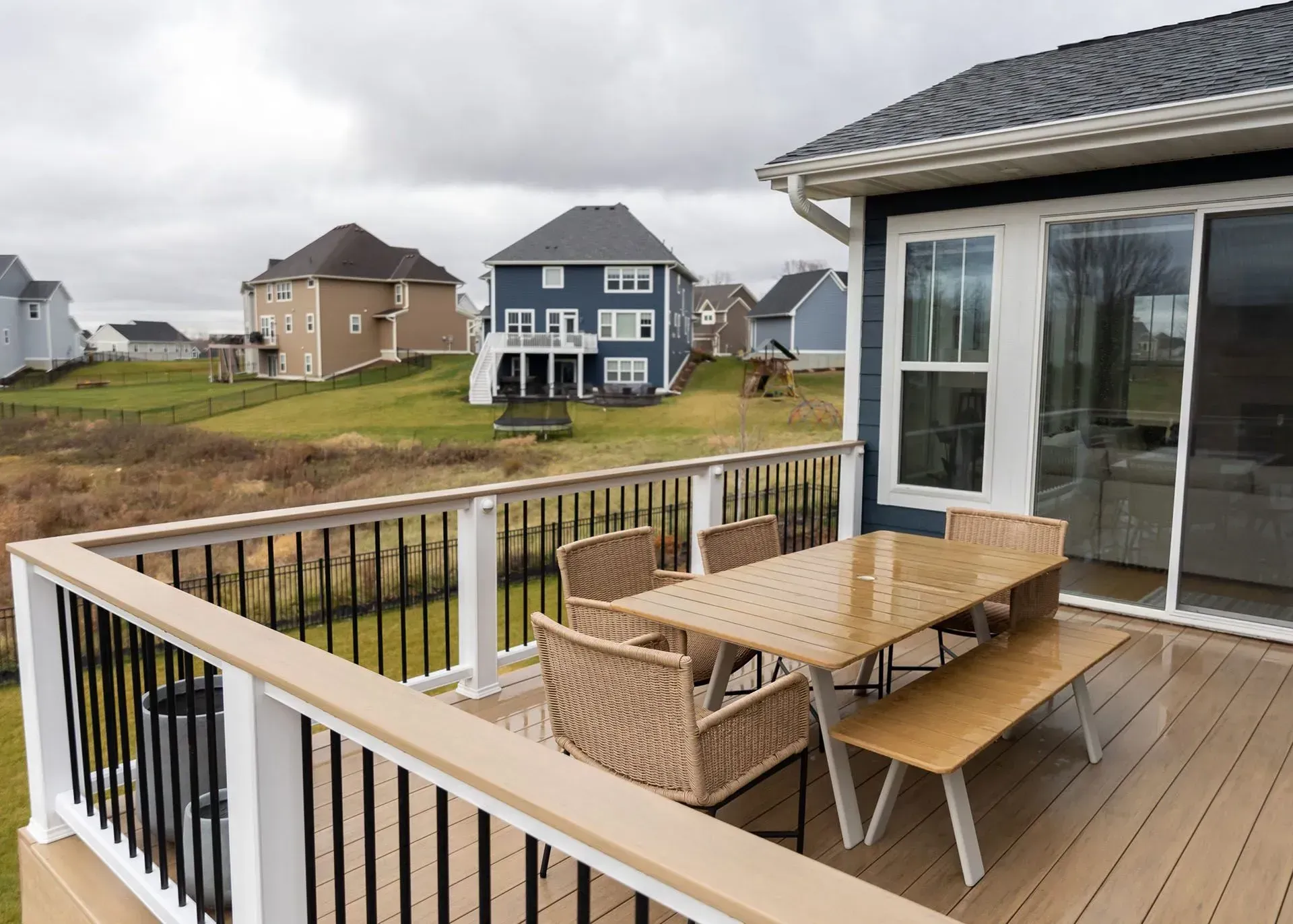 A deck with patio furniture, overlooking a grassy hill and houses, under a cloudy sky.