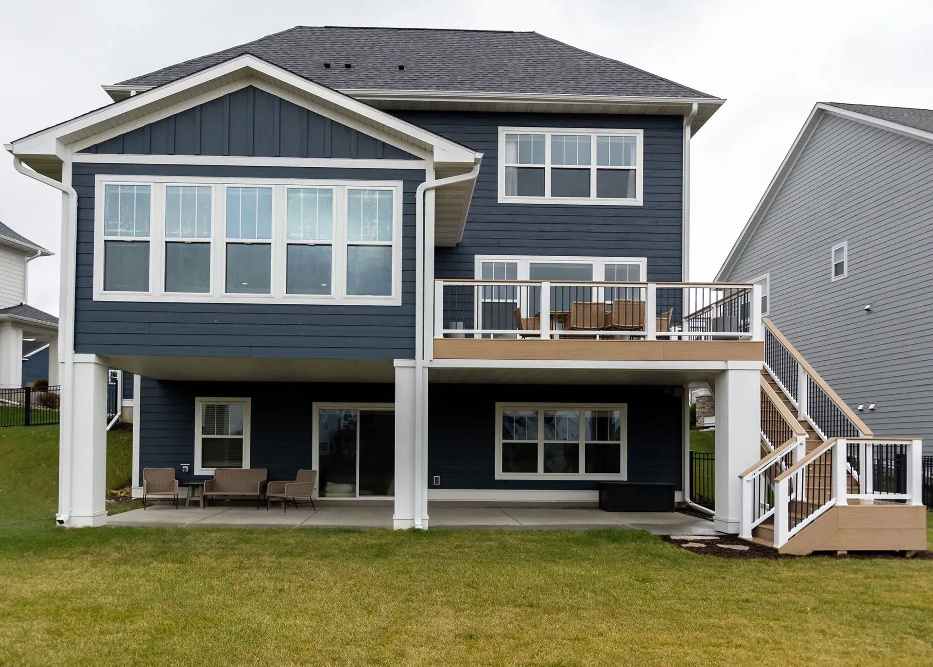 Back of a two-story blue house with white trim, deck, and stairs. Overlooks a grassy yard.