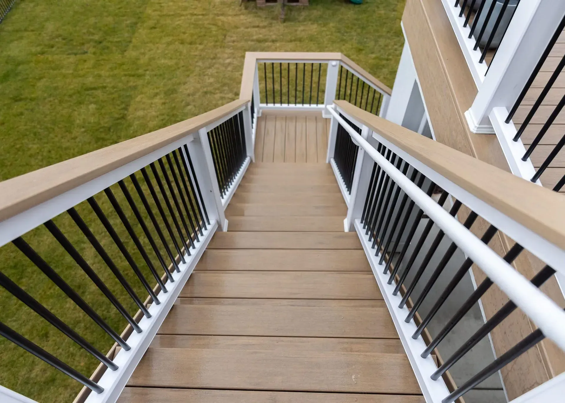 Wooden deck stairs with white railings, black vertical bars, and tan decking.