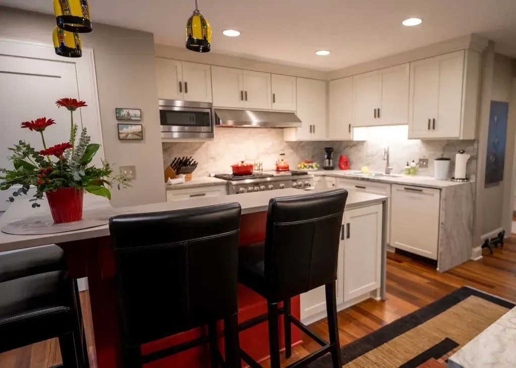 Kitchen with white cabinets, red island, stainless steel appliances, and black bar stools.