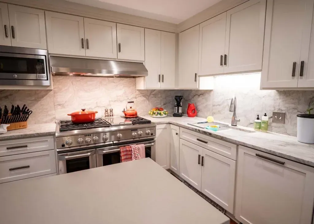 White kitchen with stainless steel appliances, marble backsplash, and a large island.