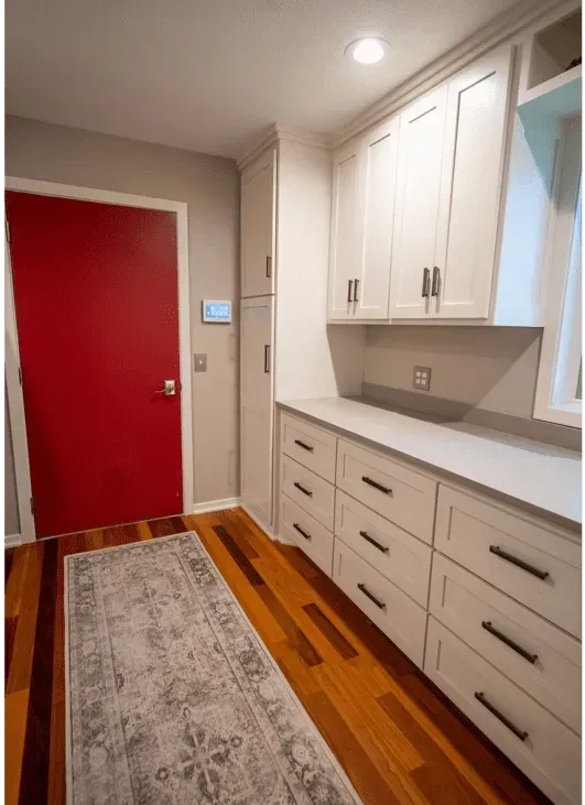 Entryway with white cabinets, red door, gray rug, and wood floor.