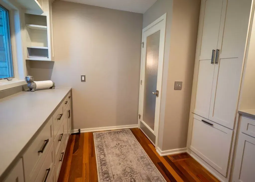 Laundry room with white cabinets, light gray walls, wood floor, and a patterned rug.