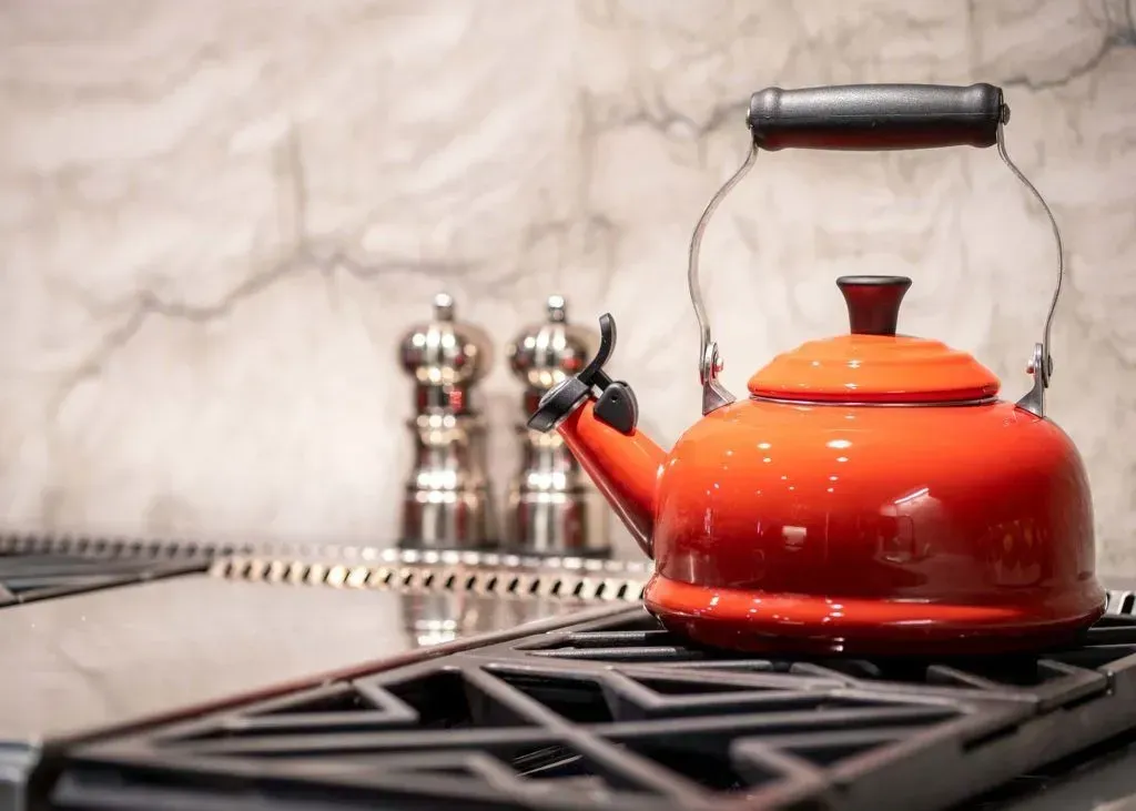 Bright orange tea kettle on a stovetop with salt and pepper shakers in the background.