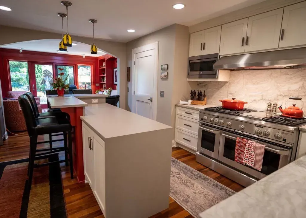 Kitchen with white cabinets, stainless steel range, island with seating, and red accent wall.