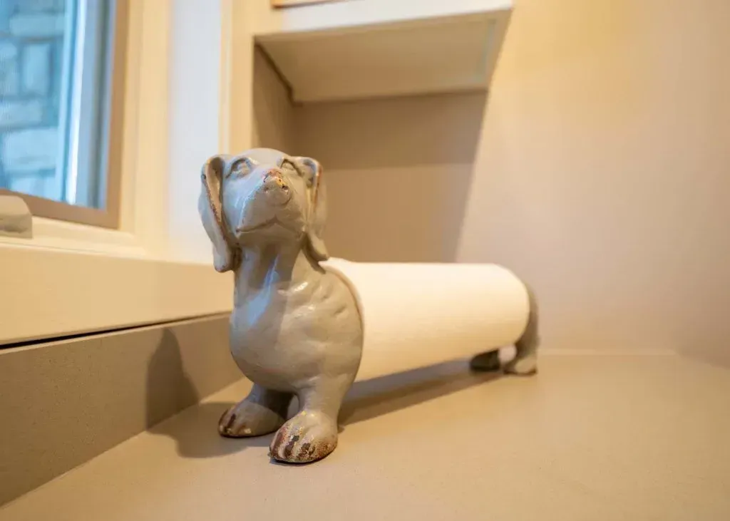Gray dachshund-shaped paper towel holder on a countertop near a window.