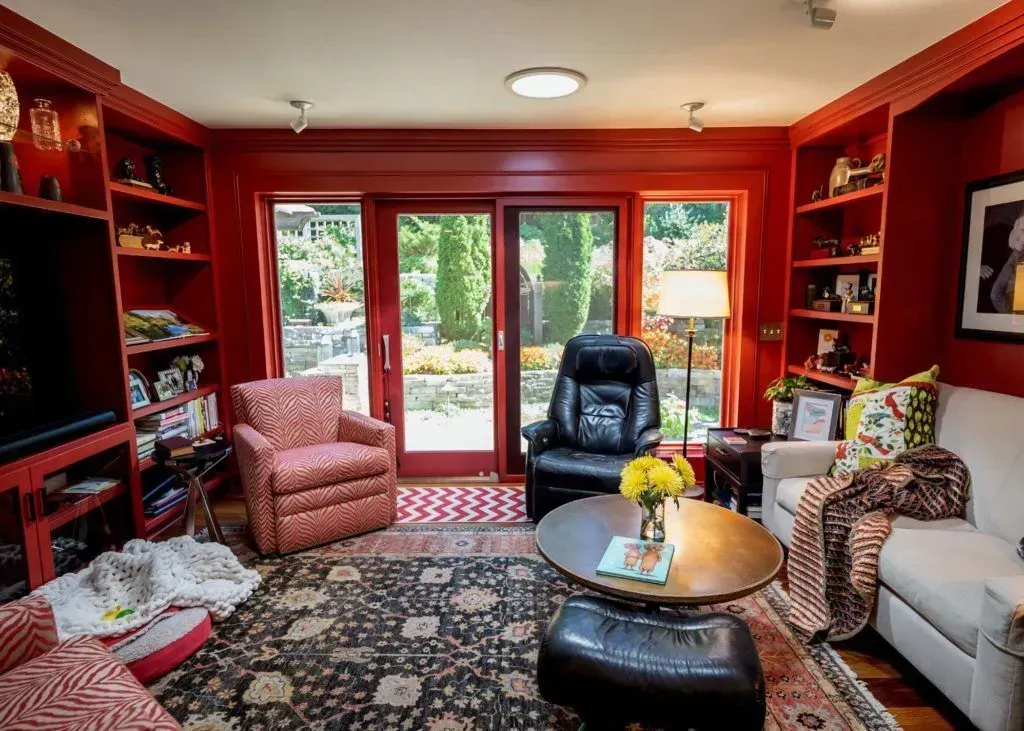 Red-walled living room with floral rug, two armchairs, a couch, and sliding glass doors to a garden.