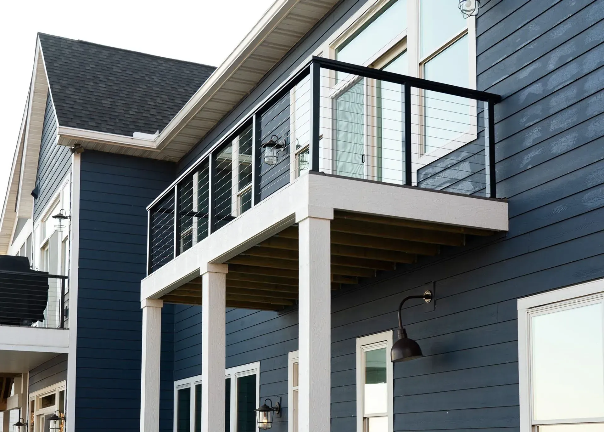 Blue house with a balcony featuring black railing and glass panels.