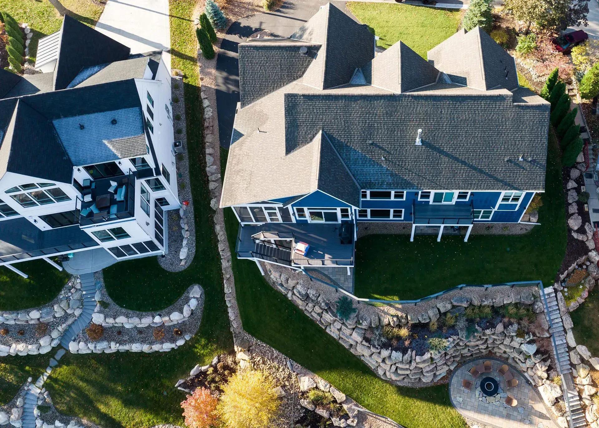 Aerial view of two modern homes with blue and white exteriors, green lawns, and stone landscaping.
