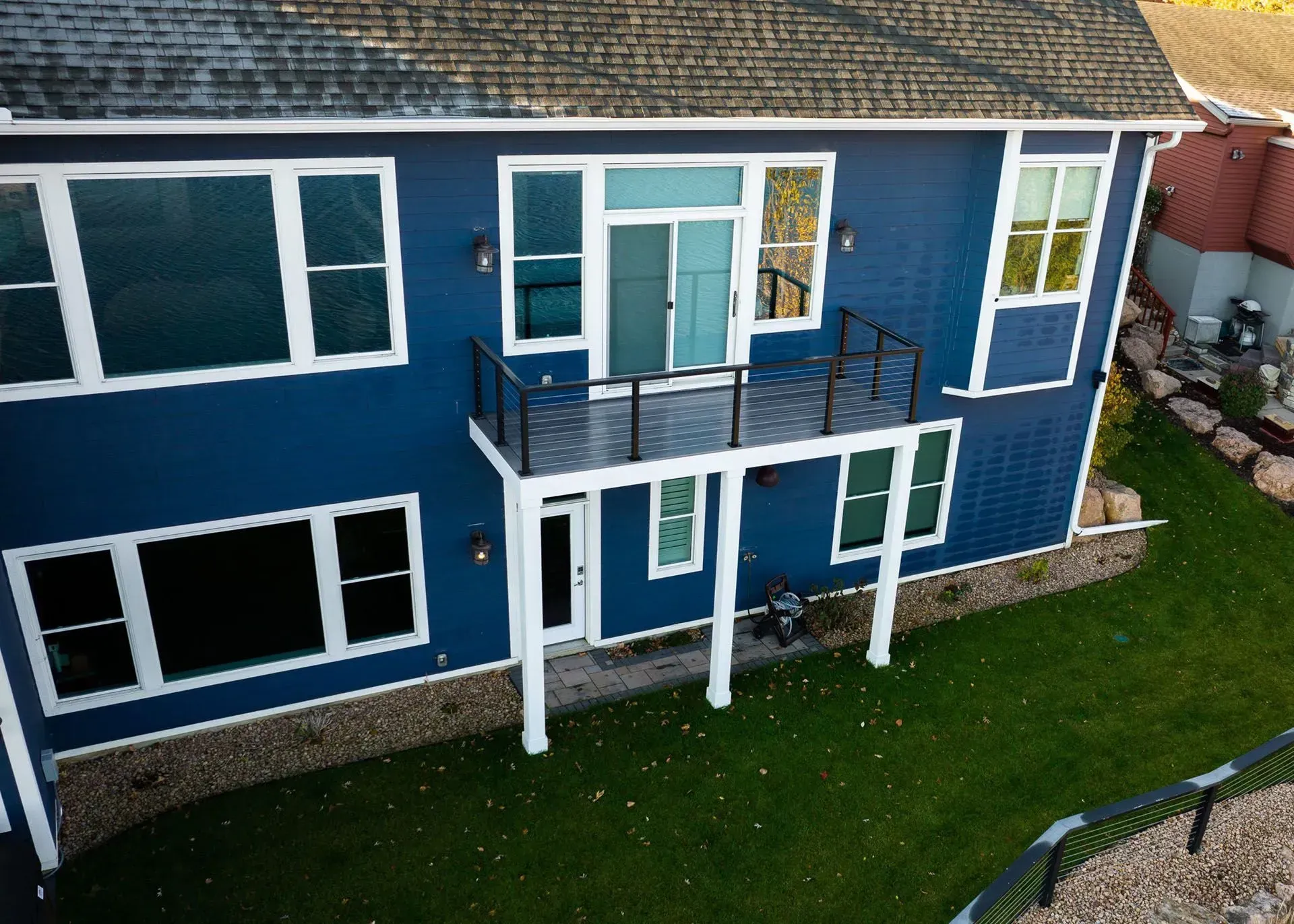 Blue two-story house with white trim, deck, and windows. Green lawn in front.