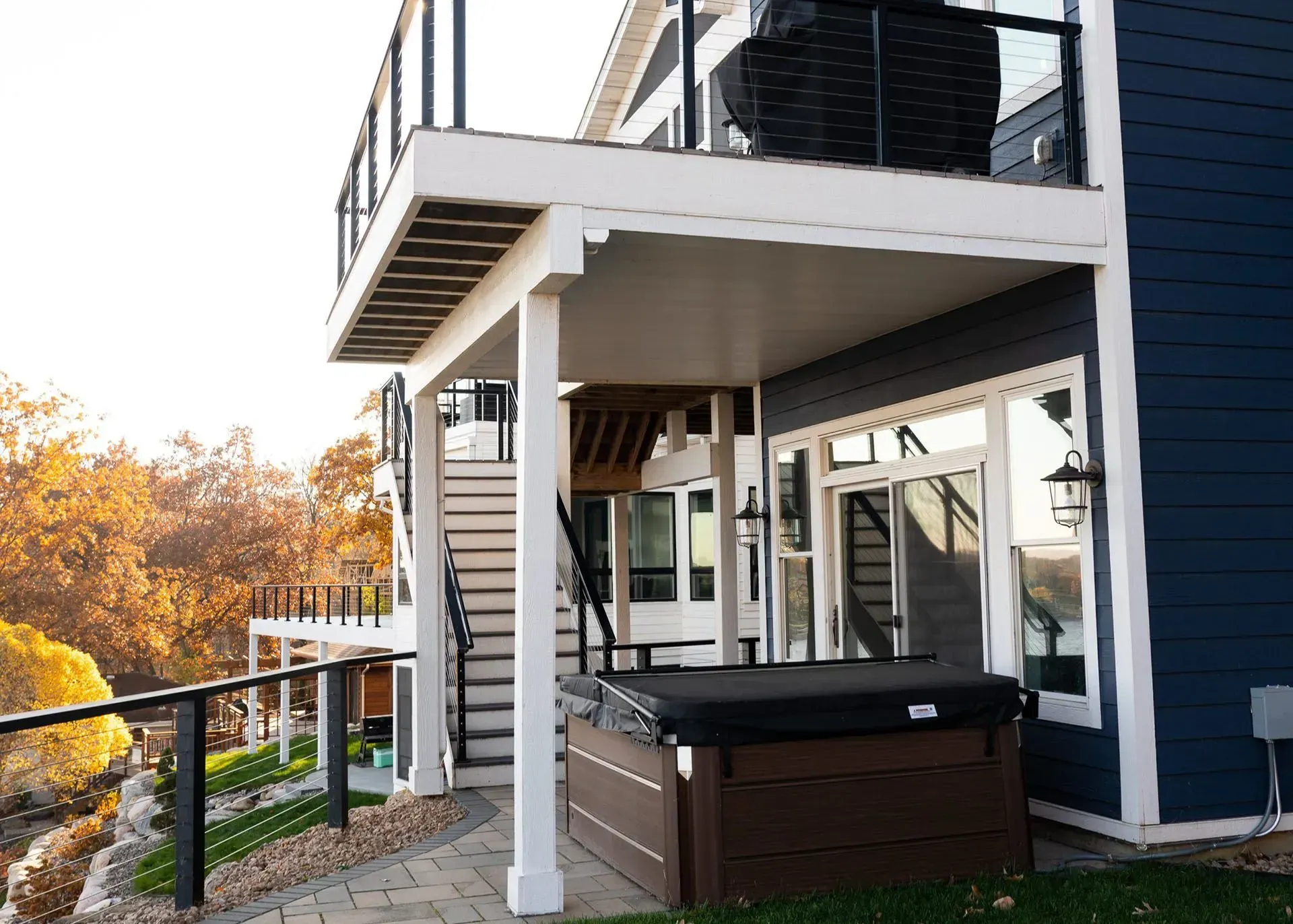 Hot tub under a deck attached to a blue house with white trim.