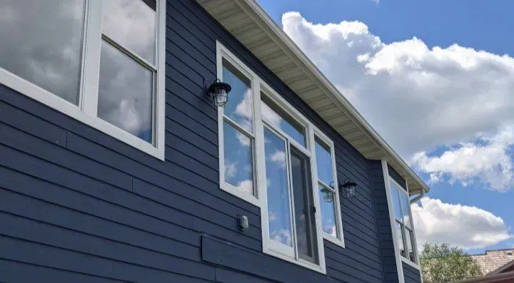 Blue house exterior with white-framed windows reflecting the sky and clouds.