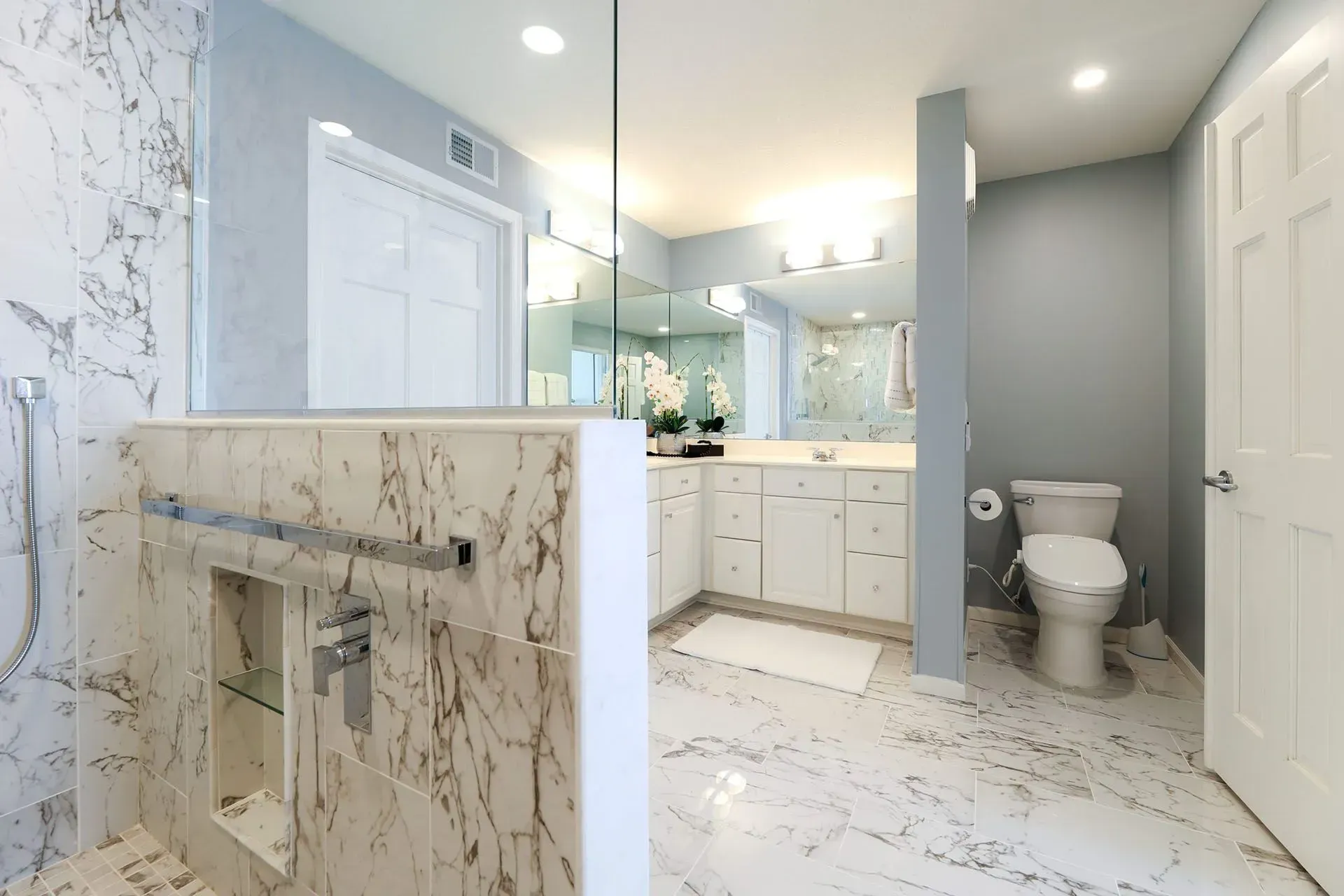 Modern bathroom with marble shower, white vanity, and blue walls.