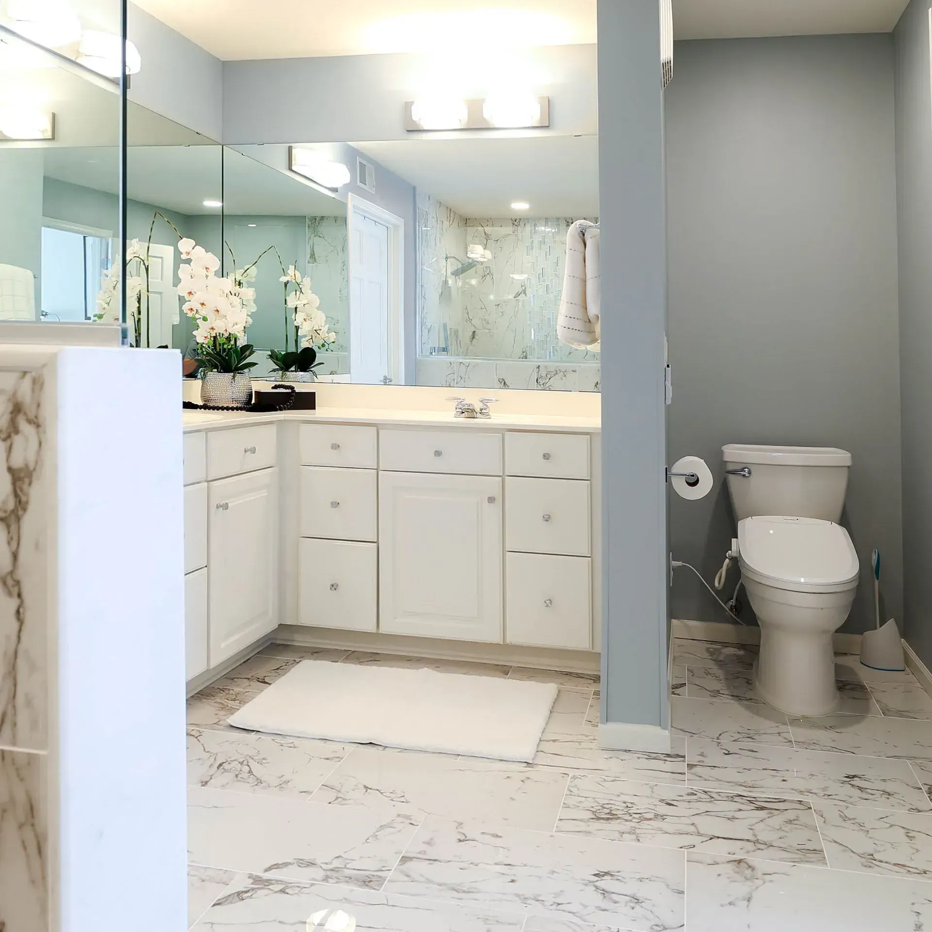 Modern bathroom with white cabinets, marble floors, and a blue wall.