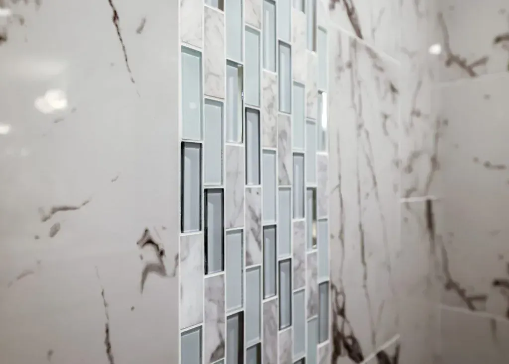 White marble tiled wall with a vertical strip of blue, gray and clear glass tiles.