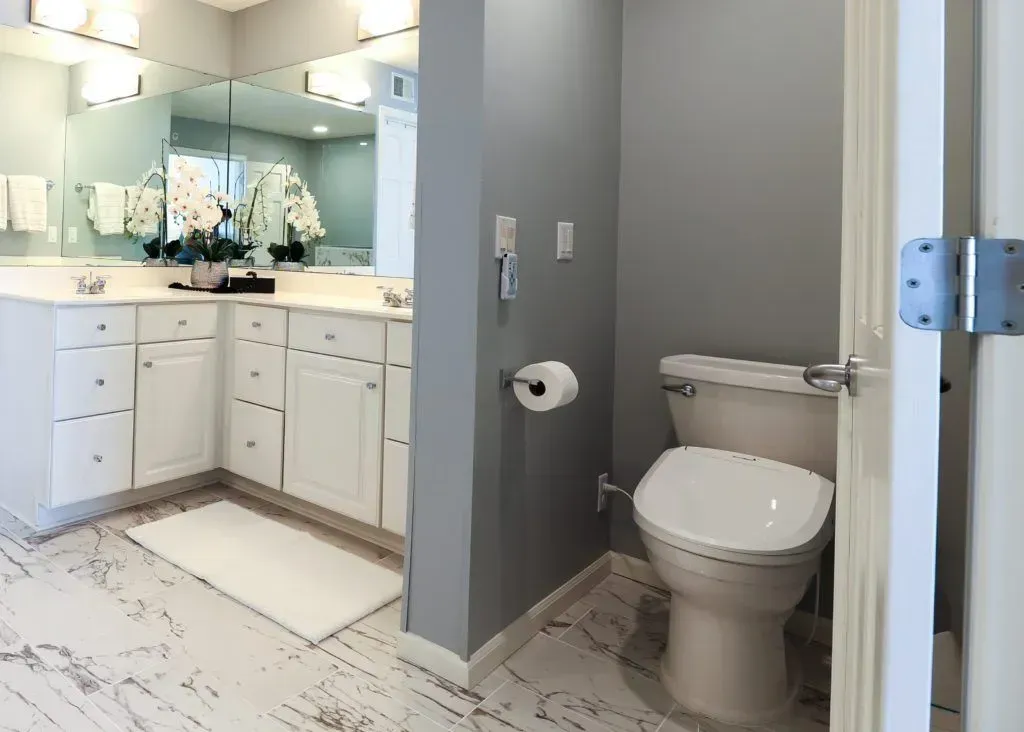 Bathroom with white vanity, toilet, and gray walls. Marble-look floor.