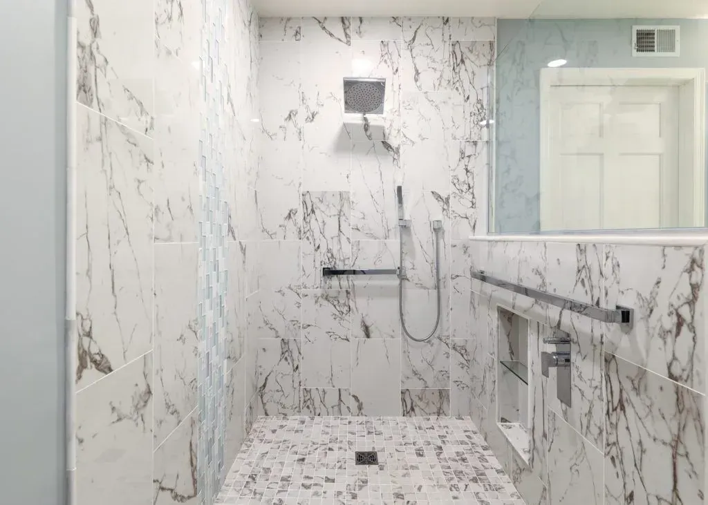 Marble-tiled shower with a hand-held showerhead and grab bar.