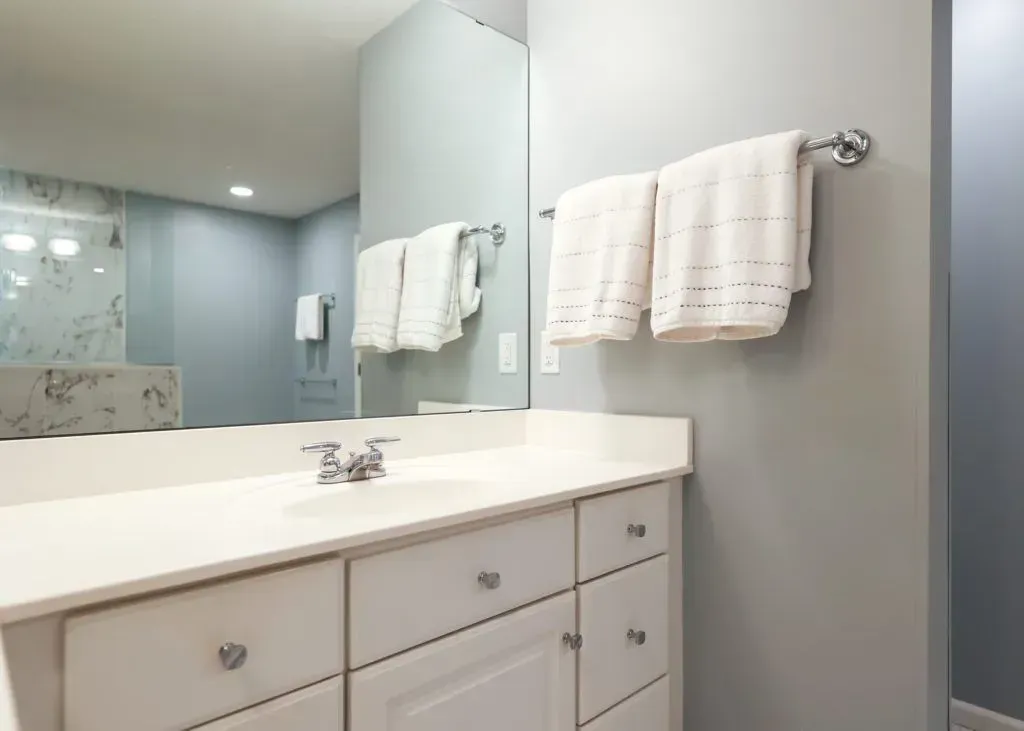 Bathroom with a white vanity, towels hanging on a chrome rack, and a large mirror reflecting the space.