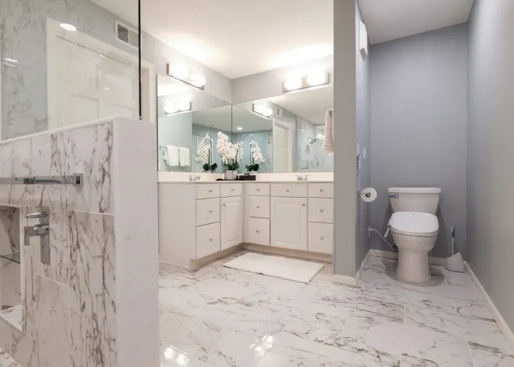 Spacious, modern bathroom with marble floors and walls, white cabinets, and a gray toilet.