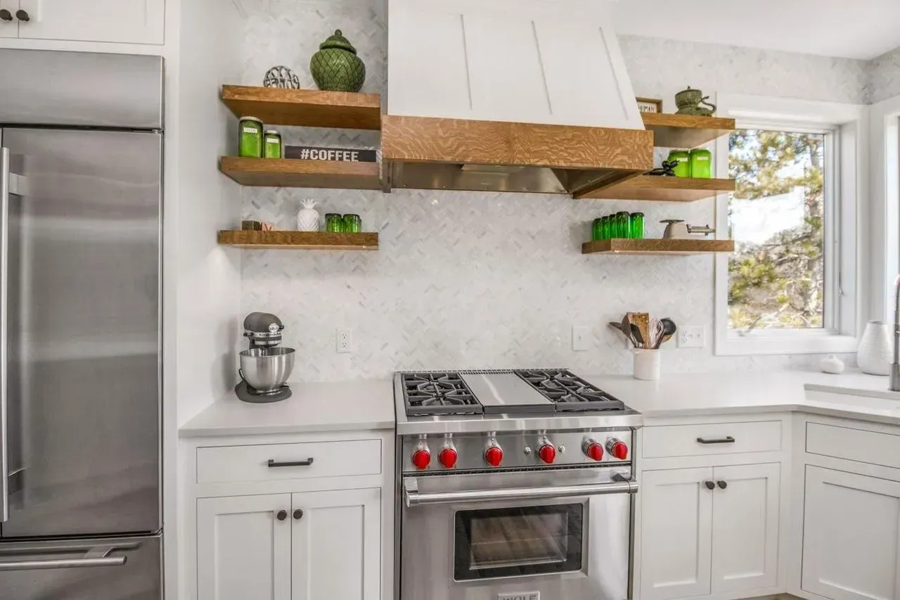 White kitchen with stainless steel appliances, open shelves, and range hood.