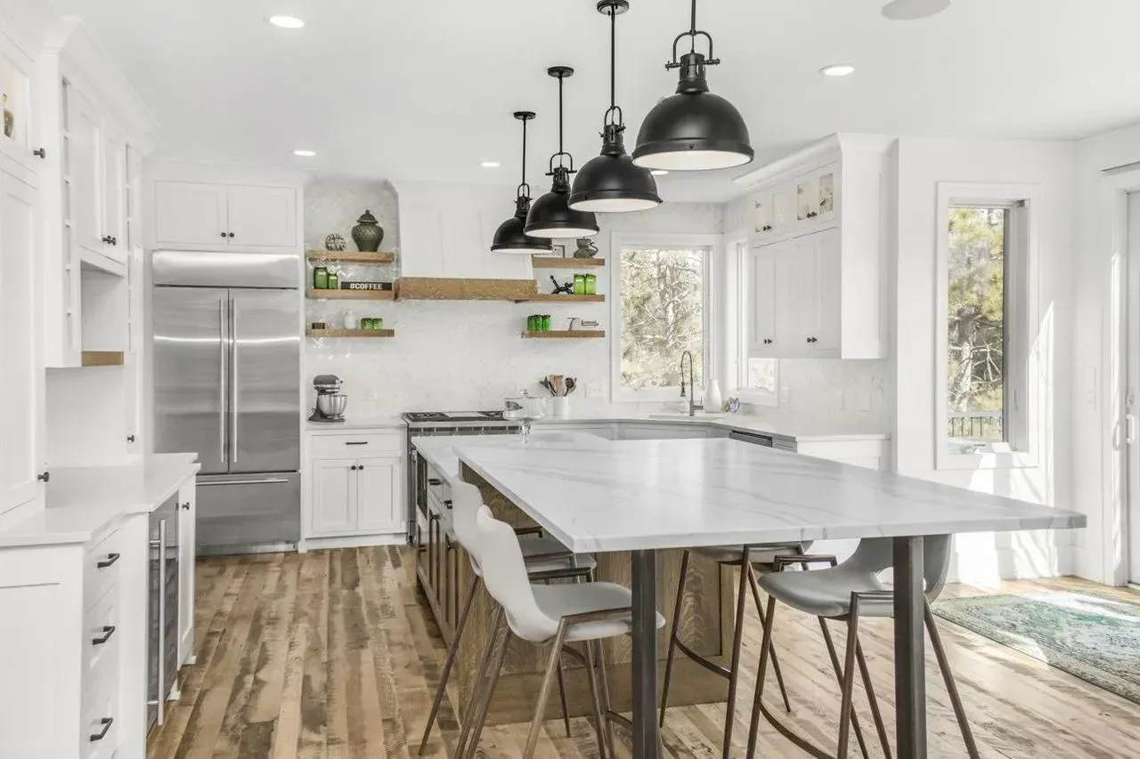 White kitchen with island, stainless steel appliances, and pendant lights.