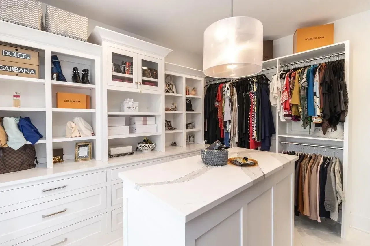 White walk-in closet with built-in shelves and an island. Clothes hanging on racks, boxes on shelves.