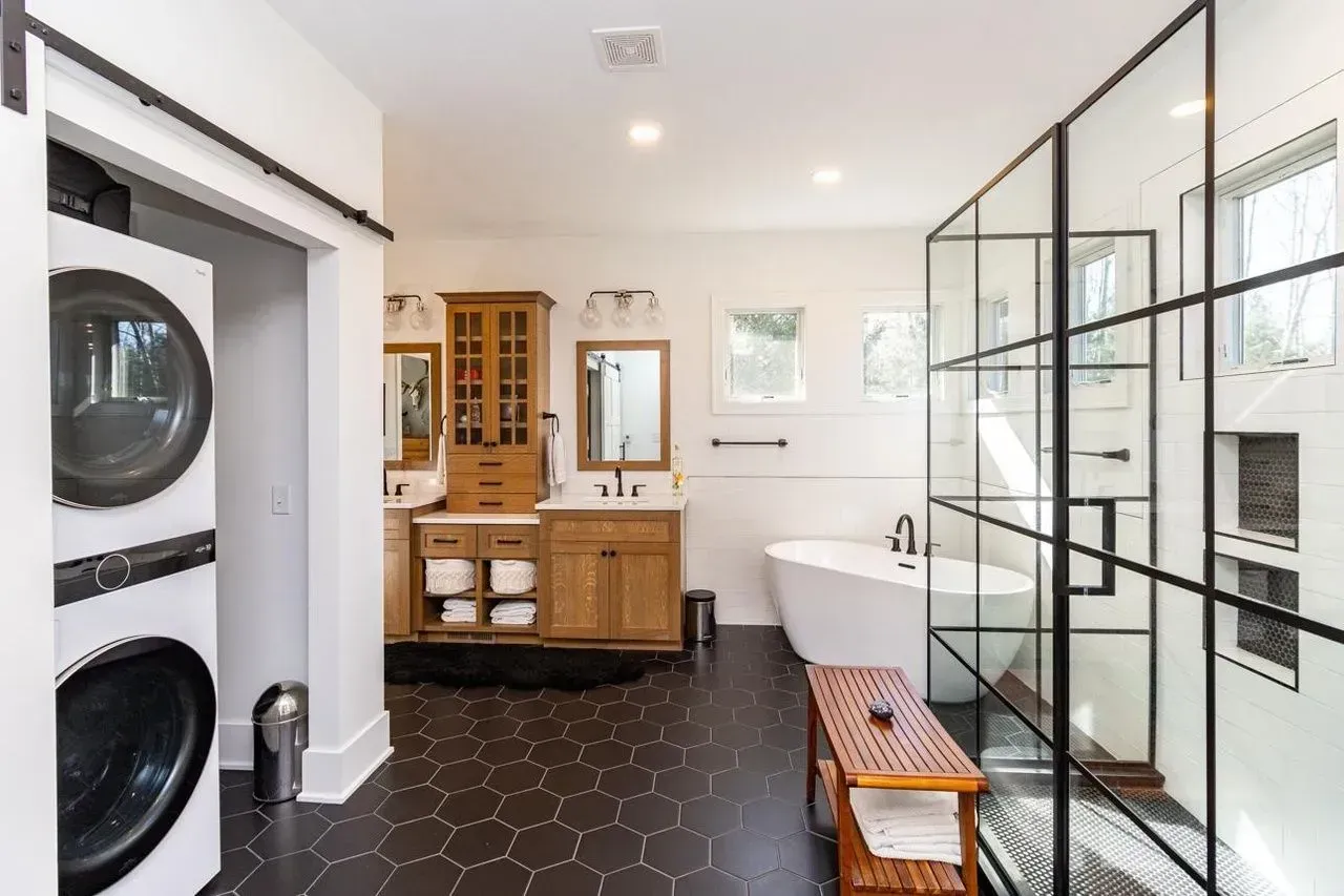 Spacious bathroom with black tile floor, glass shower, wooden cabinets, and stacked washer/dryer.