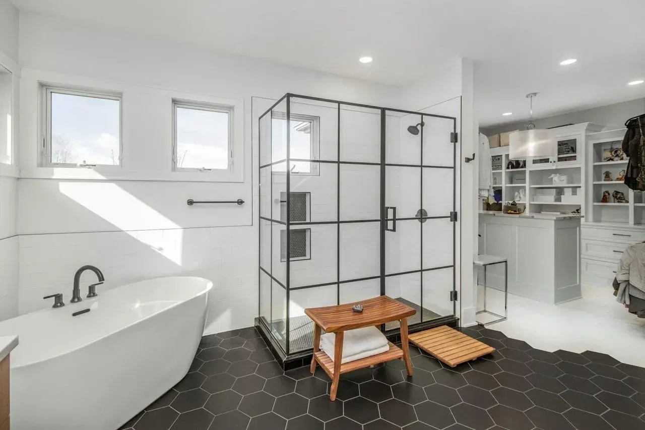 Modern bathroom with a white tub, black hexagon tile floor, and a glass-enclosed shower.