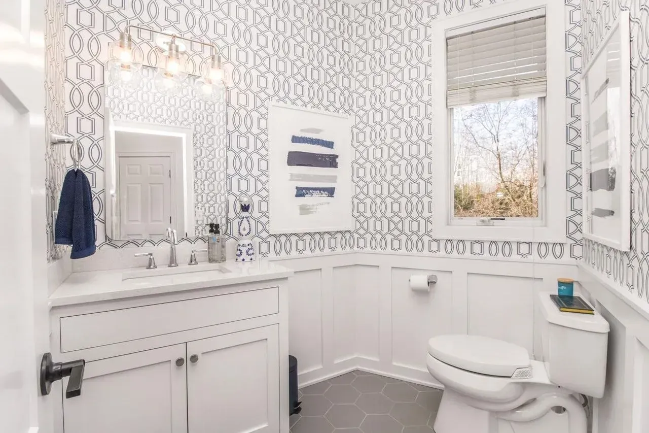White bathroom with blue patterned wallpaper and a window overlooking greenery.