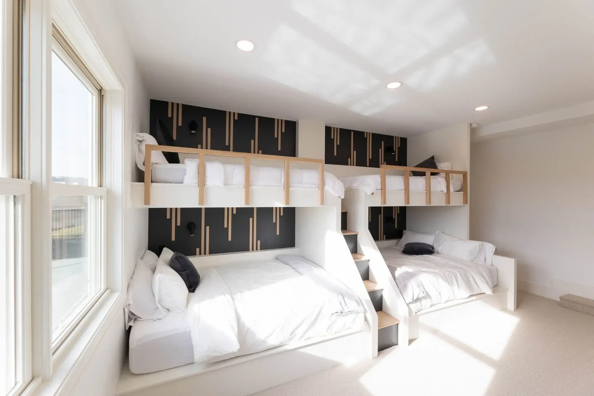 Modern bedroom with two bunk beds and a window. White walls, wood accents, and plush bedding.