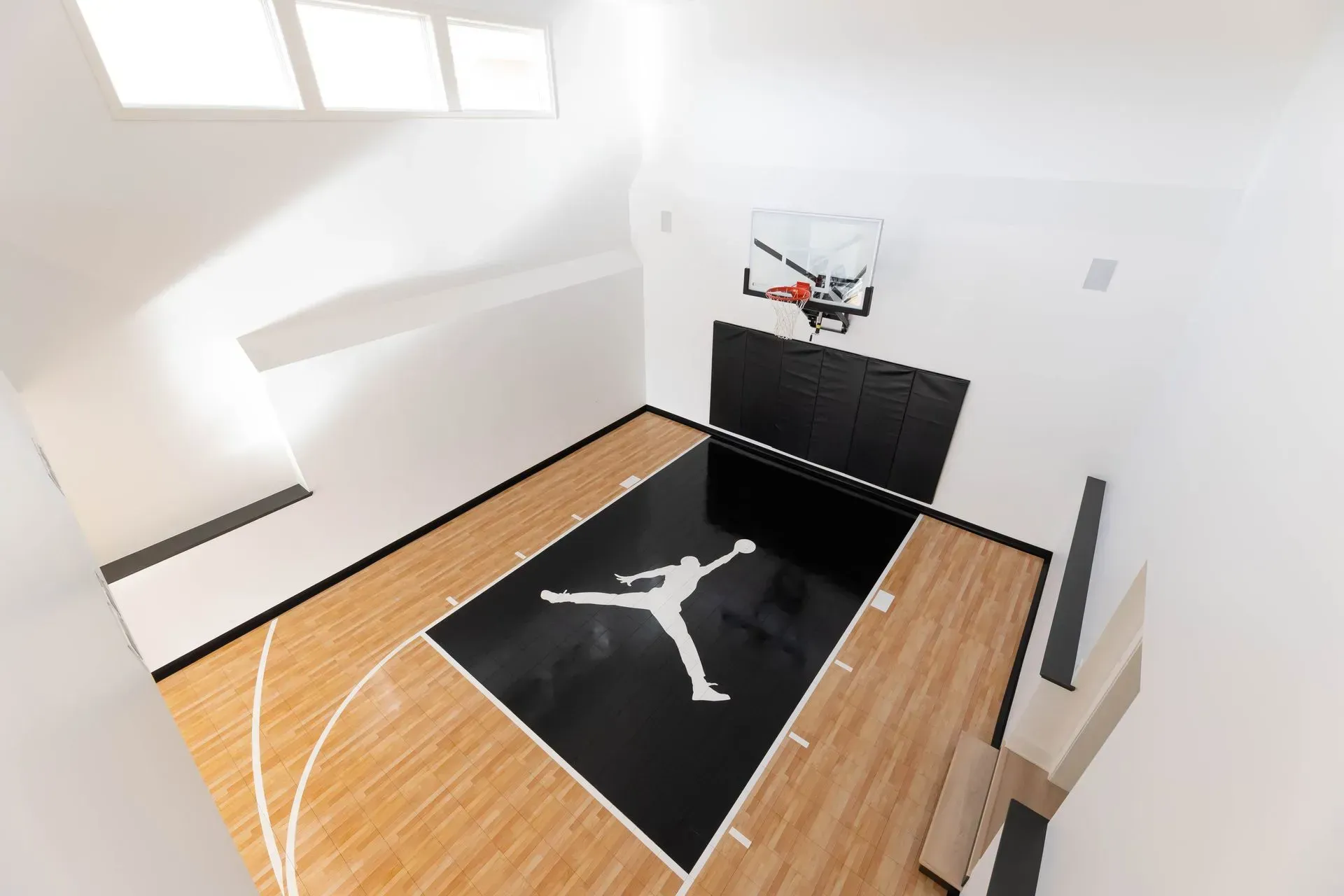 Indoor basketball court with Jordan logo, black and wood flooring, white walls, hoop.