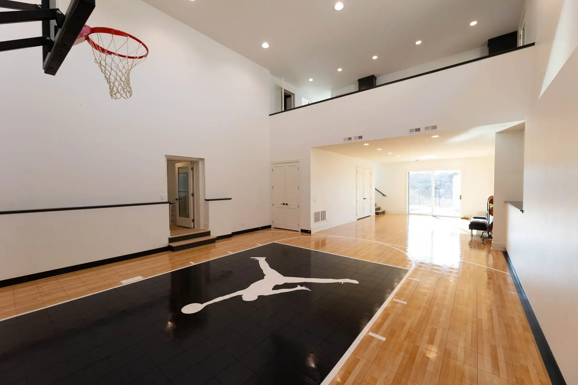 Basketball court with black and white floor and Jordan logo, hoop, and loft area.